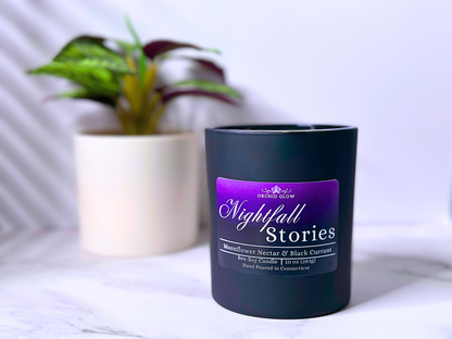 A black candle jar with a purple label that reads 'Nightfall Stories', with a white plant pot in the background.