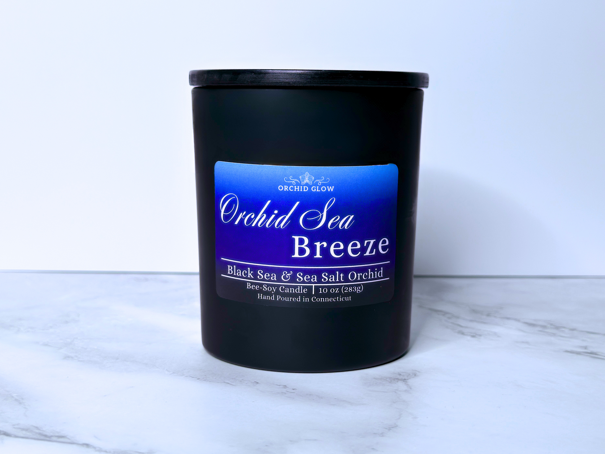 A black candle jar with a label reading 'Orchid Sea Breeze', placed on a marble surface.