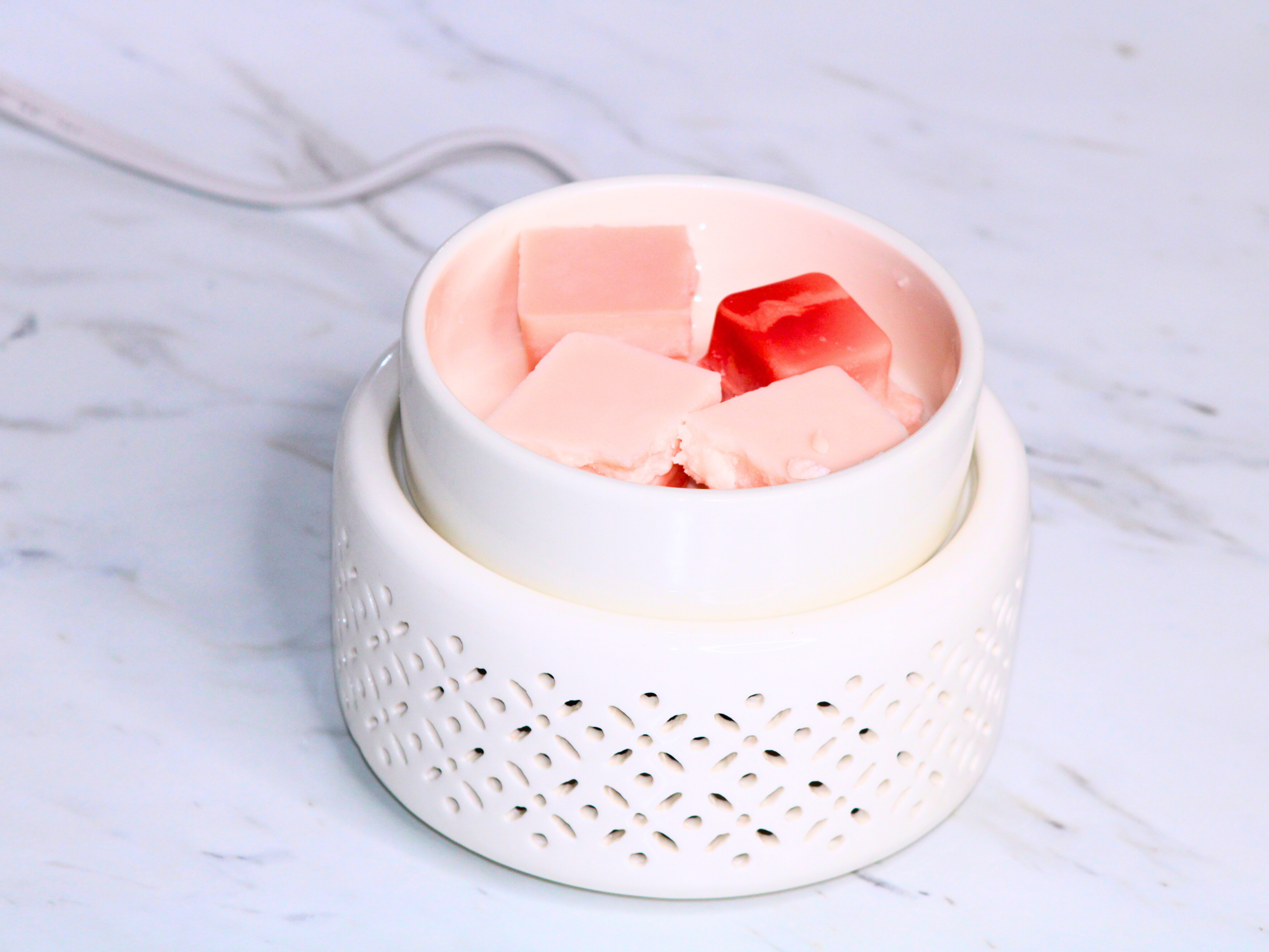 White wax warmer with light orange and orange wax cubes on a marble surface